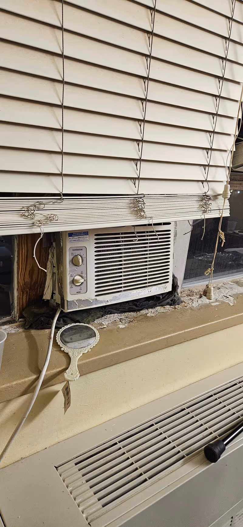 Exterior view of beige window blinds with a wall-mounted air conditioner