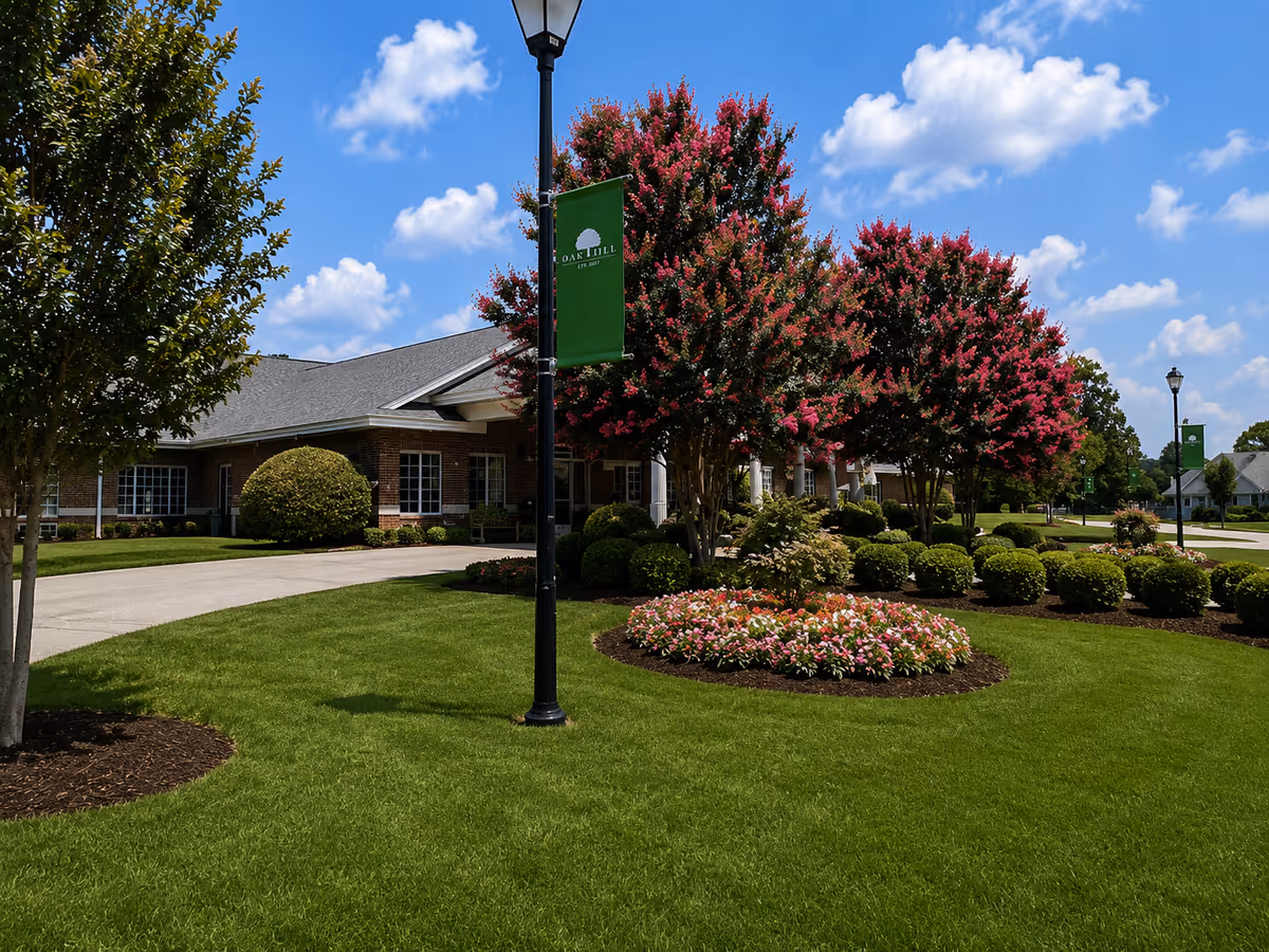 Exterior view of Oak Hill Assisted Living Community with manicured lawn, trees, and flower beds.