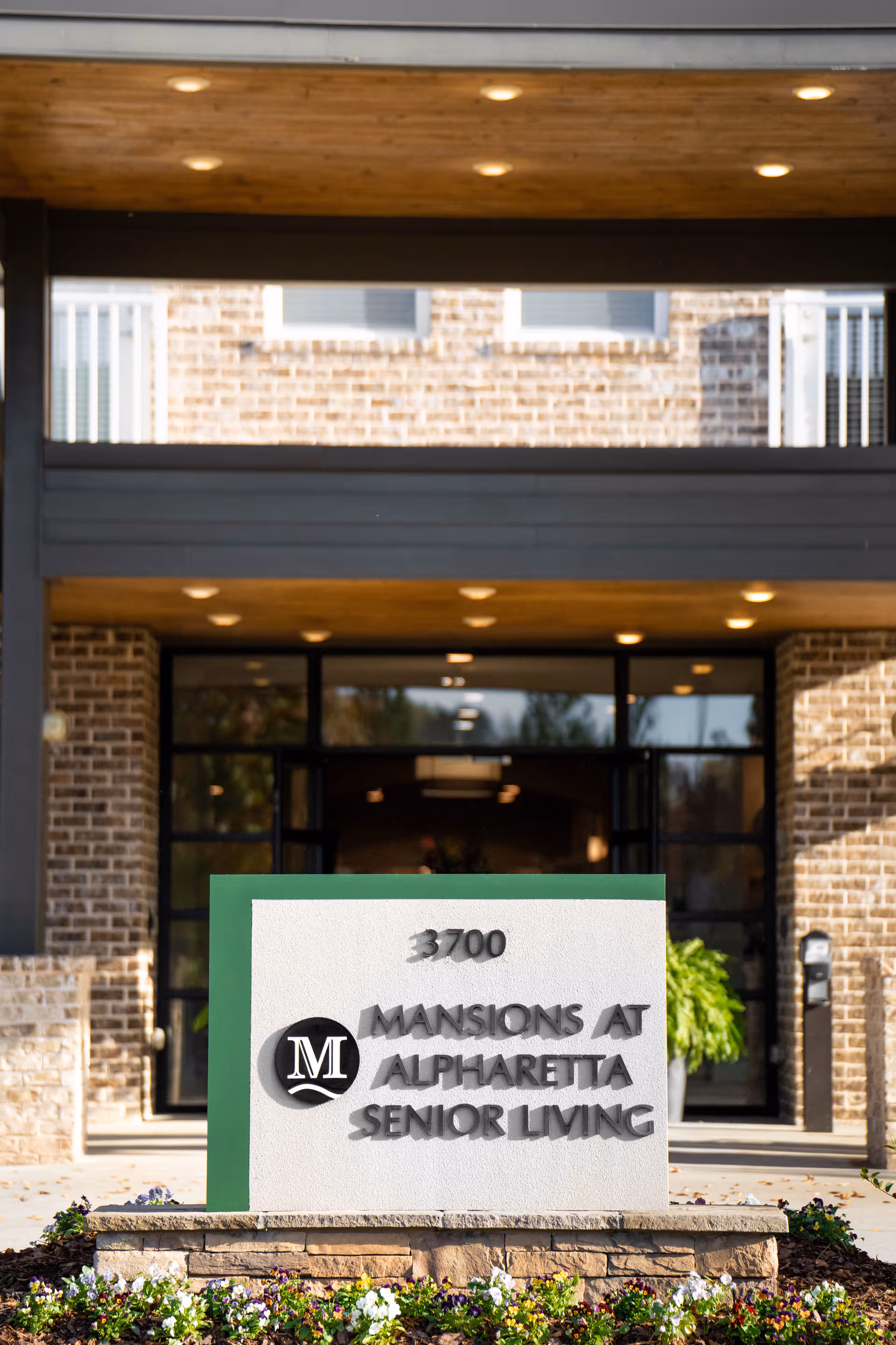 Front entrance of The Mansions at Alpharetta Senior Living with sign and landscaping.