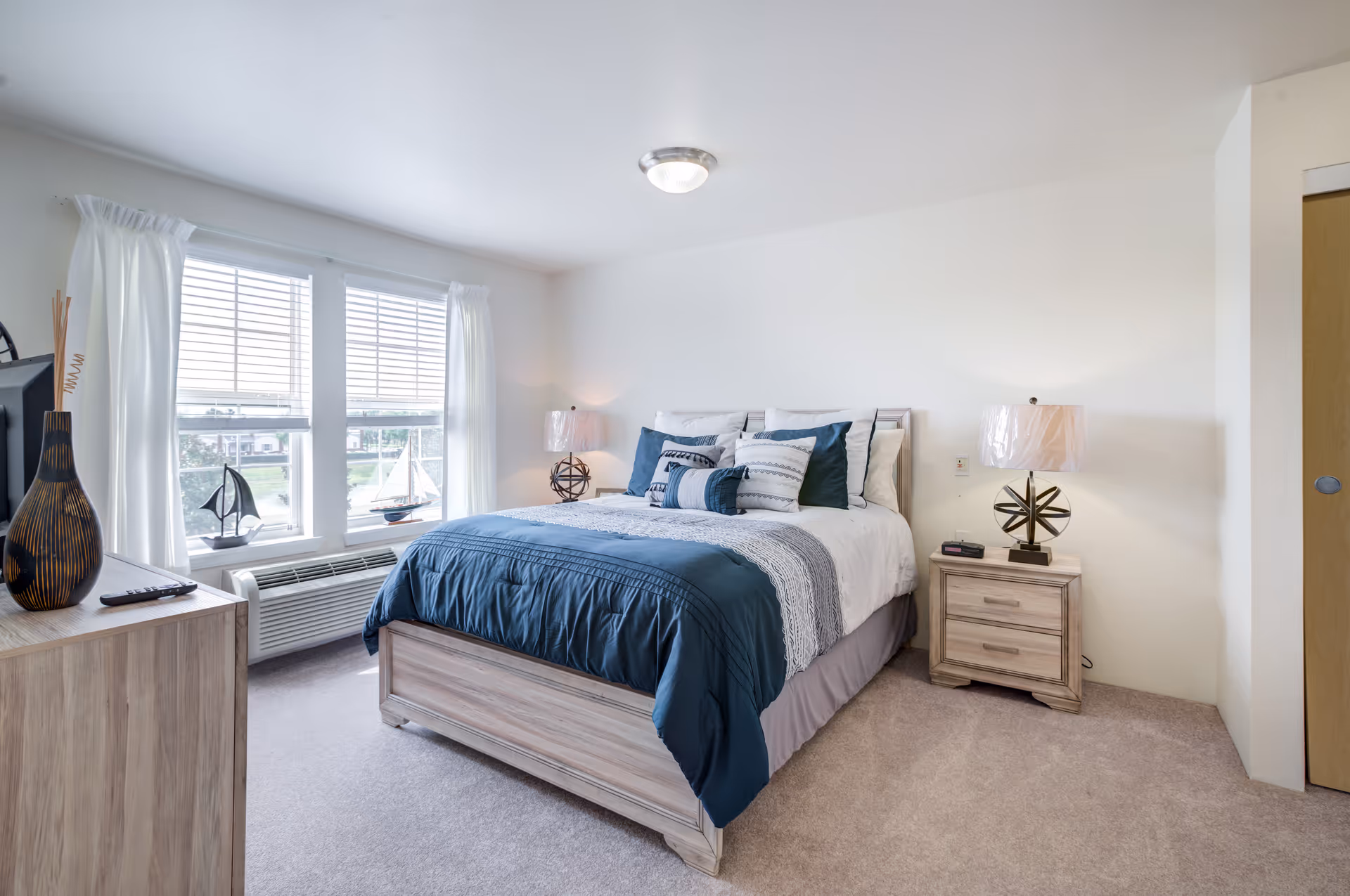 A tidy bedroom with a blue bedspread, pillows, and matching bedside lamps.