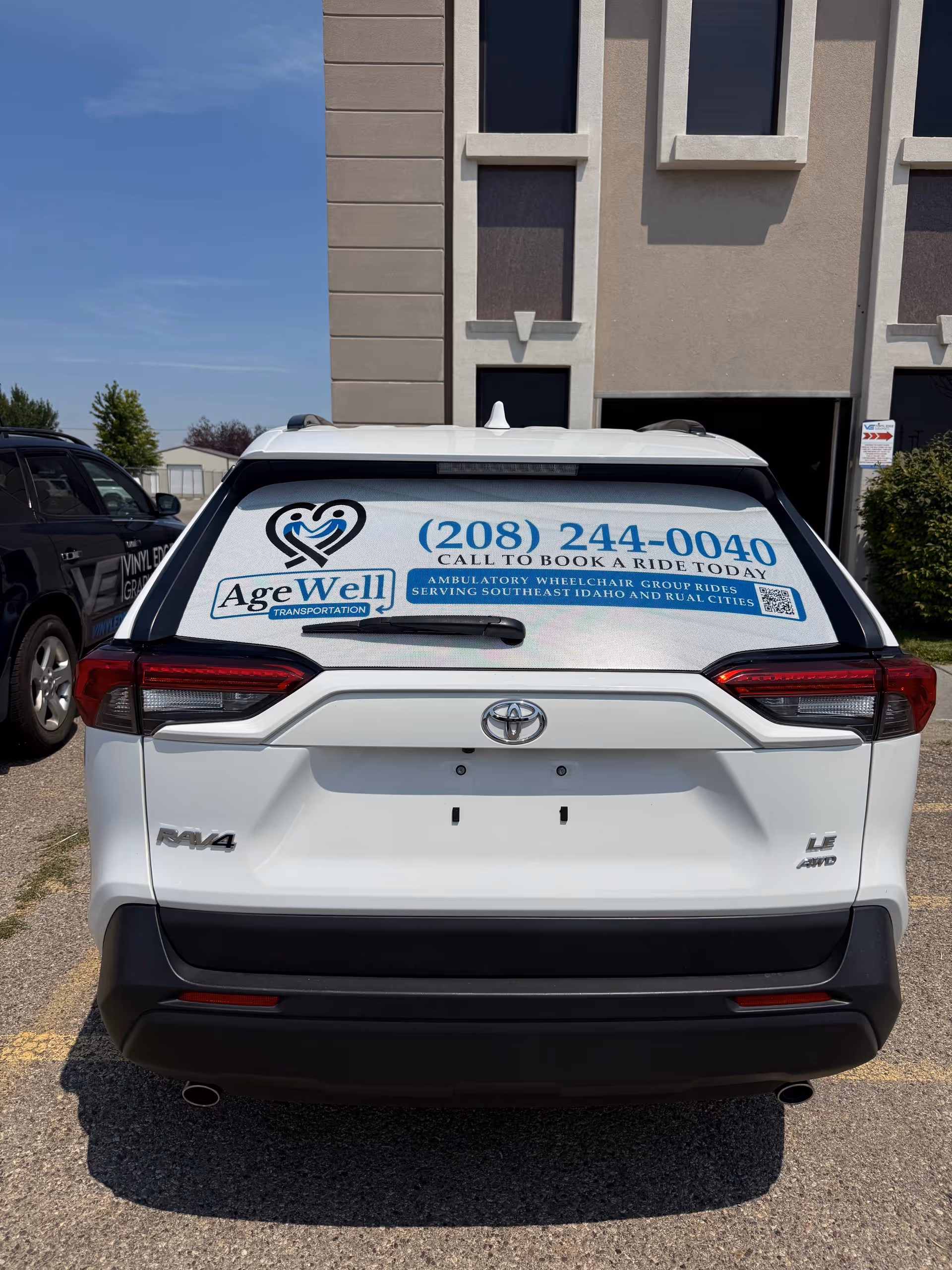 White Toyota SUV with AgeWell branding and phone number parked in front of a beige building.