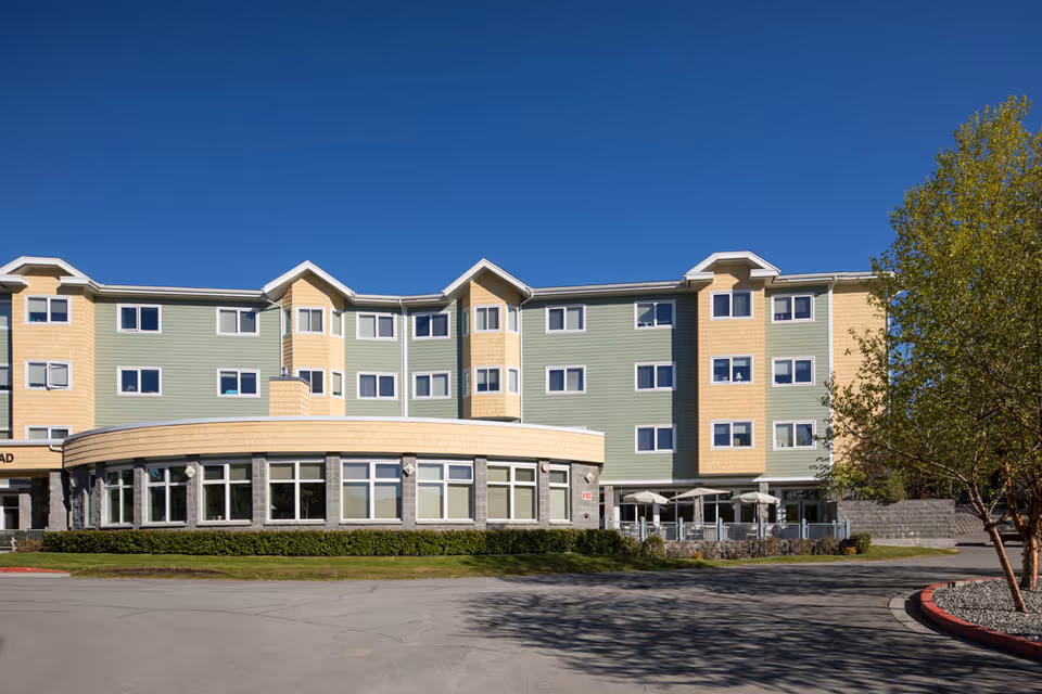 Colorful multi-story senior living facility with curved glass entrance and outdoor seating.