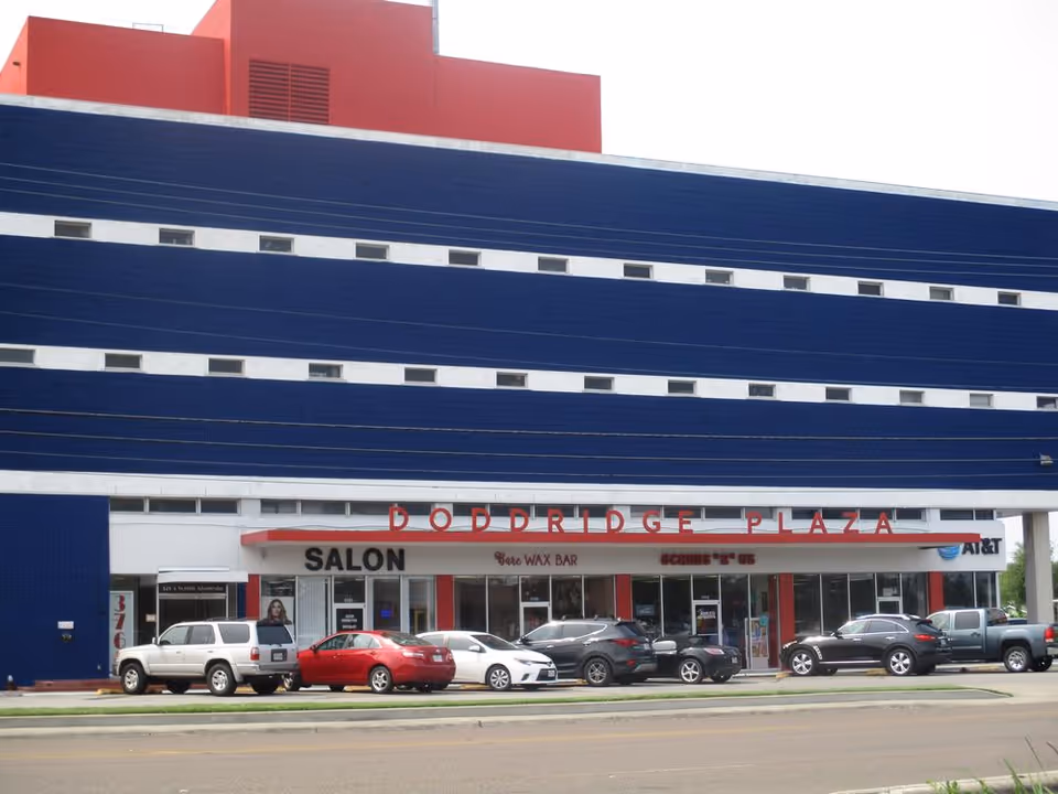 Front view of Boddridge Plaza, a large blue building with a red top and parked cars.