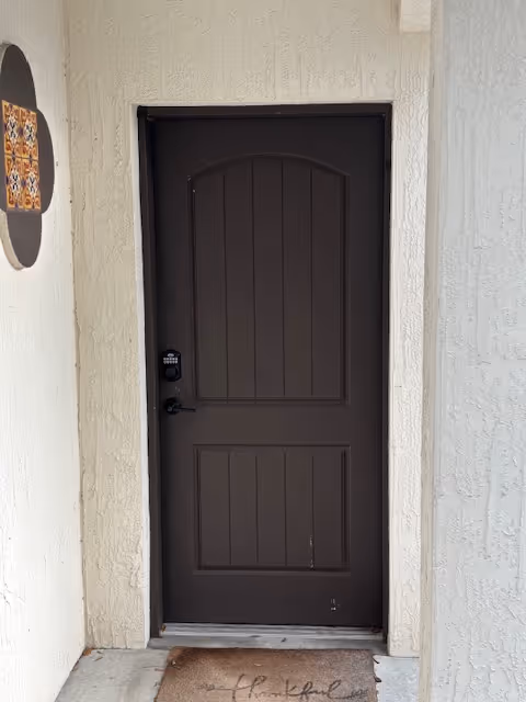 Dark brown door with keypad lock on a textured light wall and a doormat.