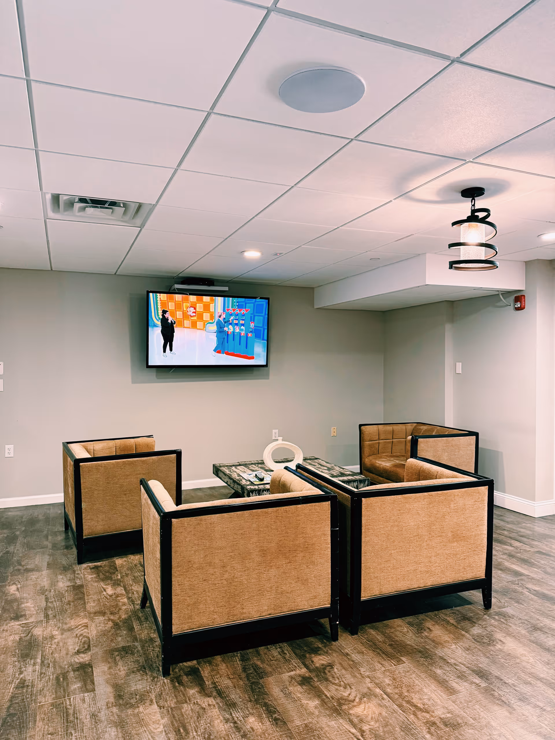 Small lounge area with four armchairs around a coffee table facing a wall-mounted TV.