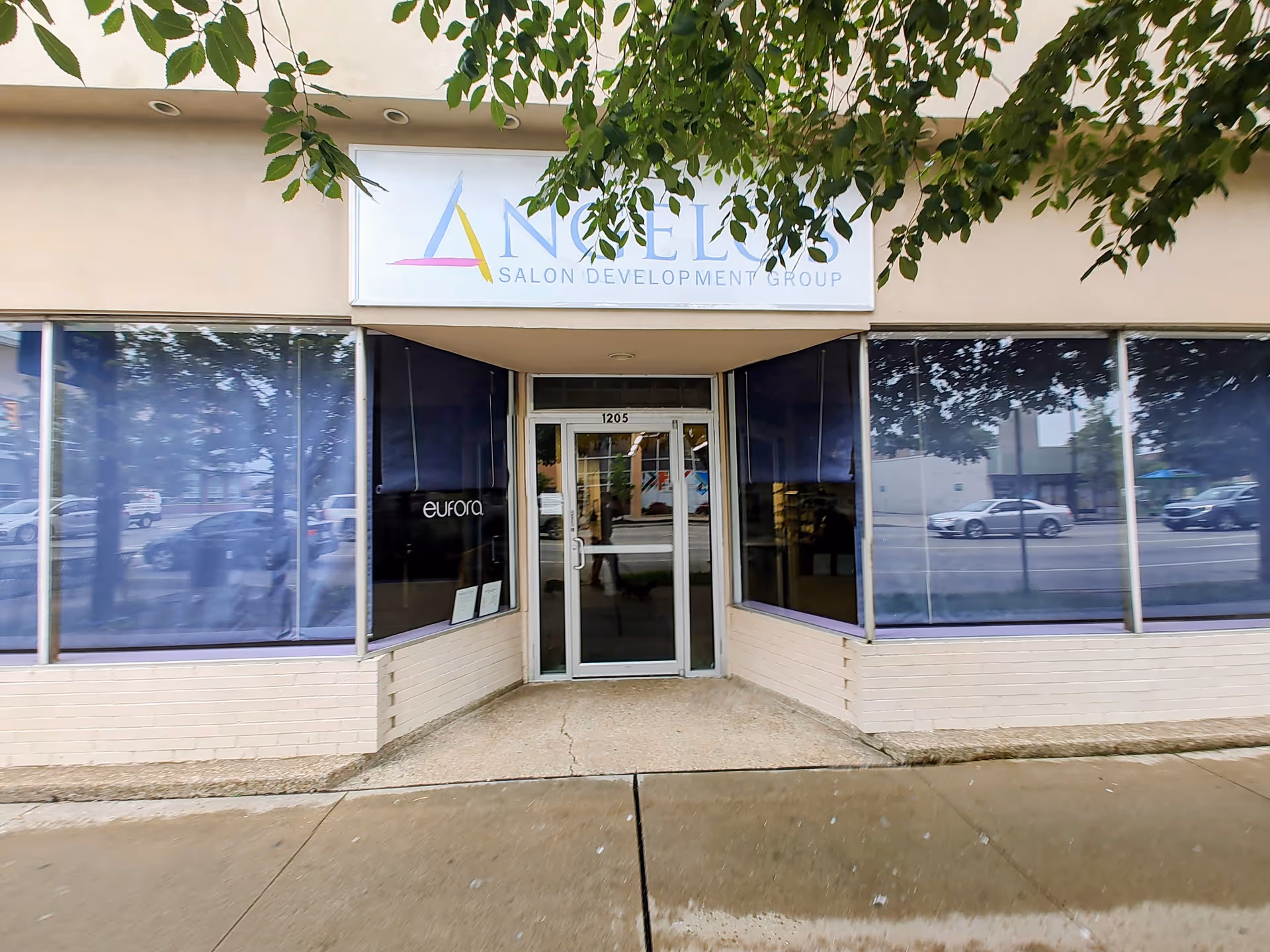 Front entrance of a beige storefront with large glass windows and a sign overhead.