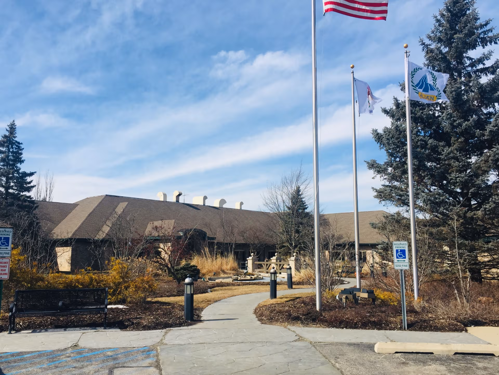 Alden Estates of Barrington exterior view with flags, trees, and a walkway to the entrance.