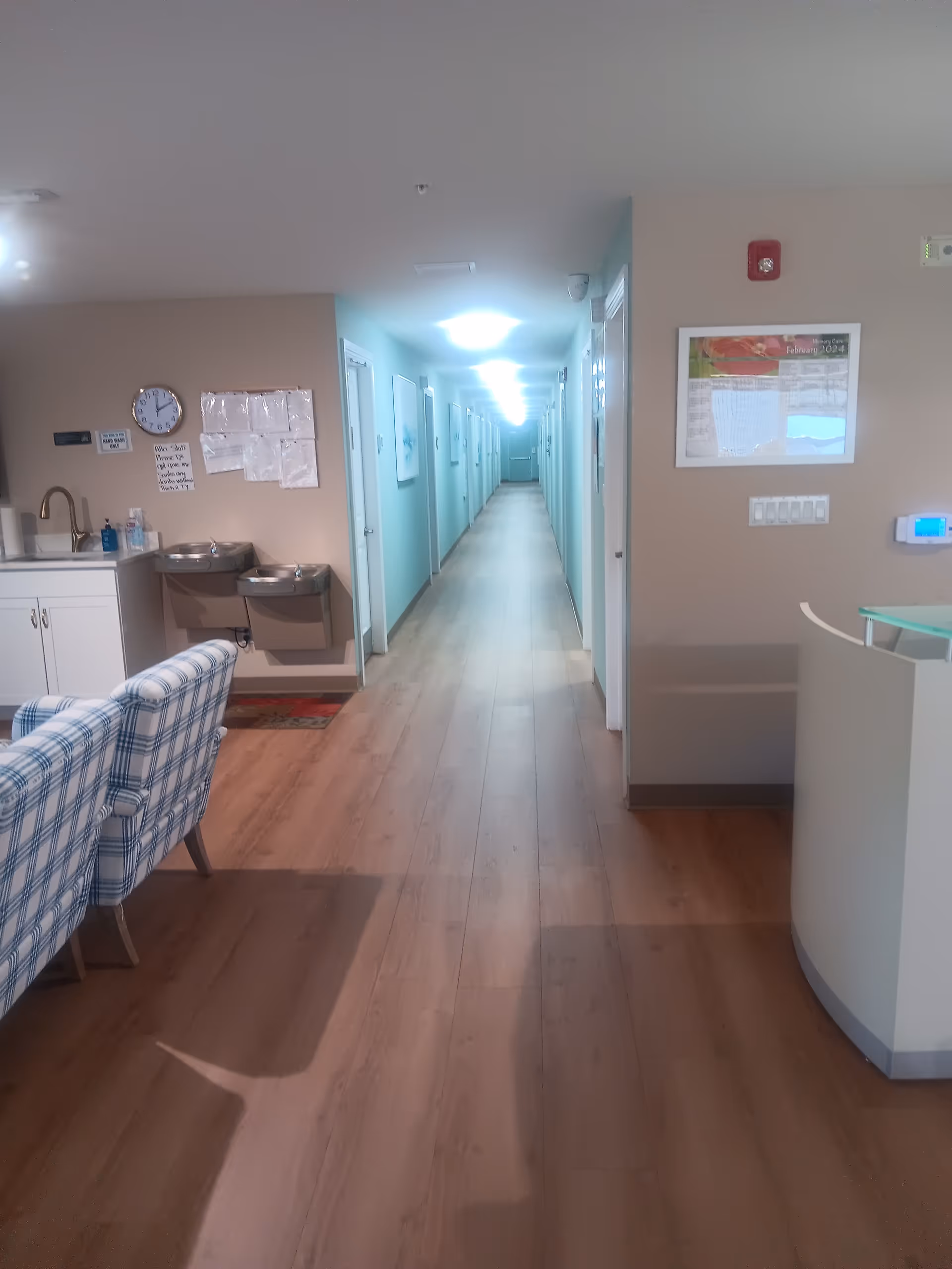 Long corridor in a senior living facility with turquoise walls and seating area.