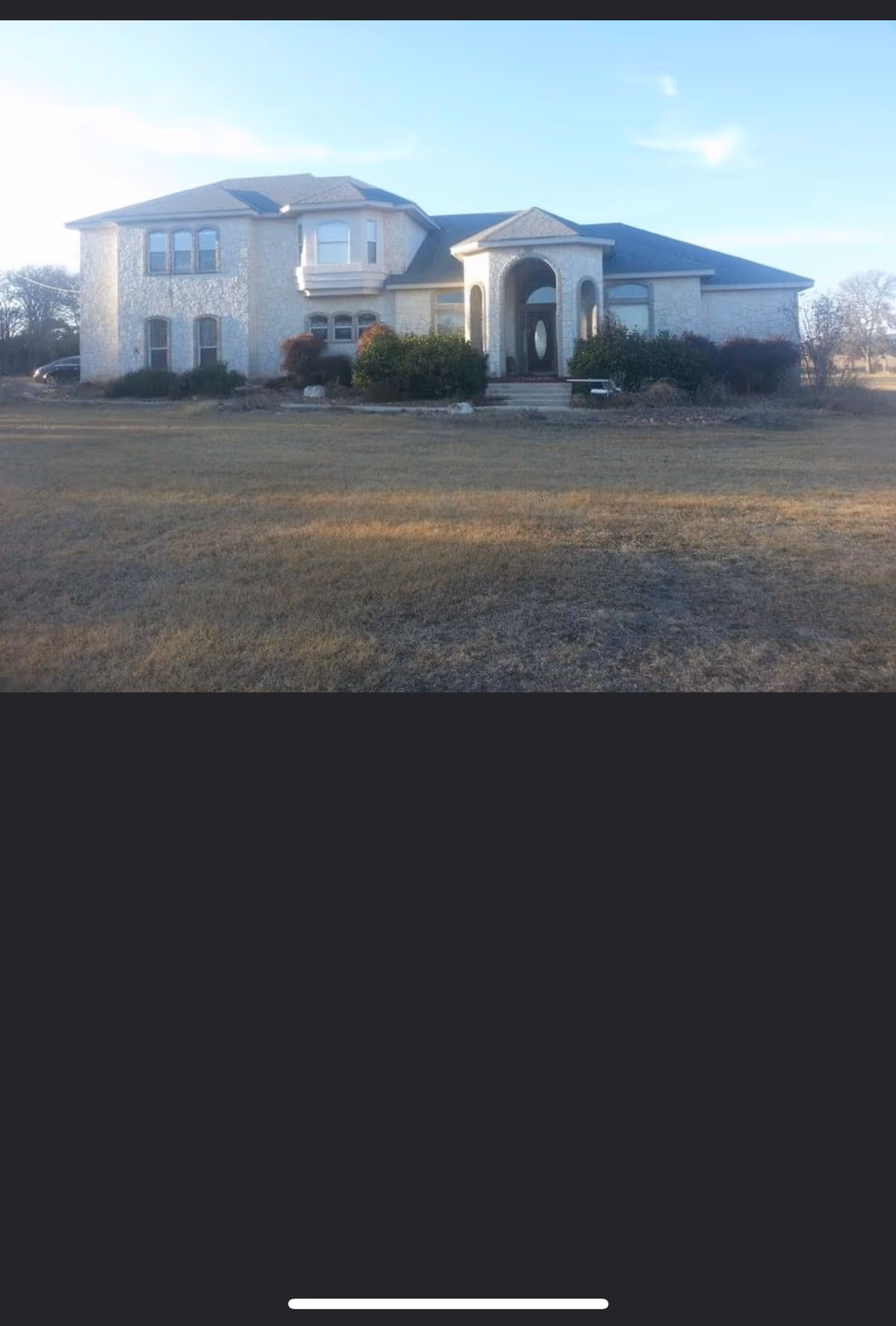 Two-story light-colored building with arched entry and landscaped front yard.