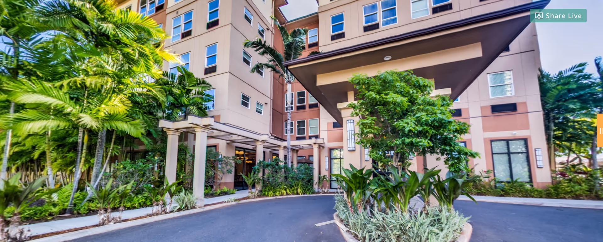 Entrance and porte-cochere of a multi-story senior living building surrounded by tropical landscaping and palm trees.