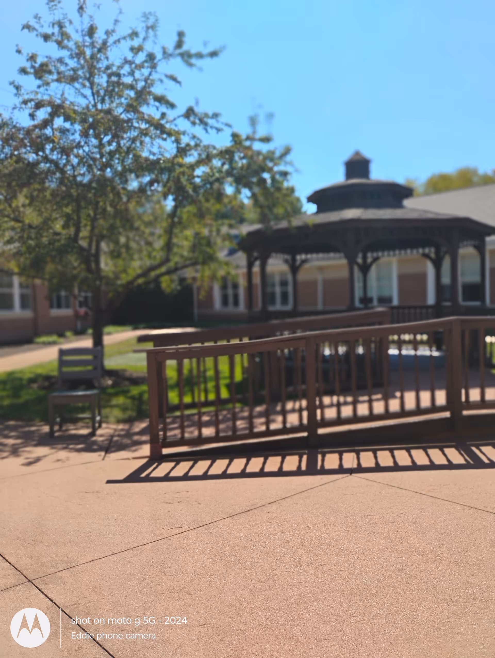 Outdoor courtyard with a gazebo, railing, and mature trees near a brick senior living building.