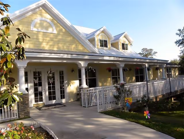 Yellow Magnolia Manor Assisted Living exterior with a covered front porch, white railings, and welcoming entrance.