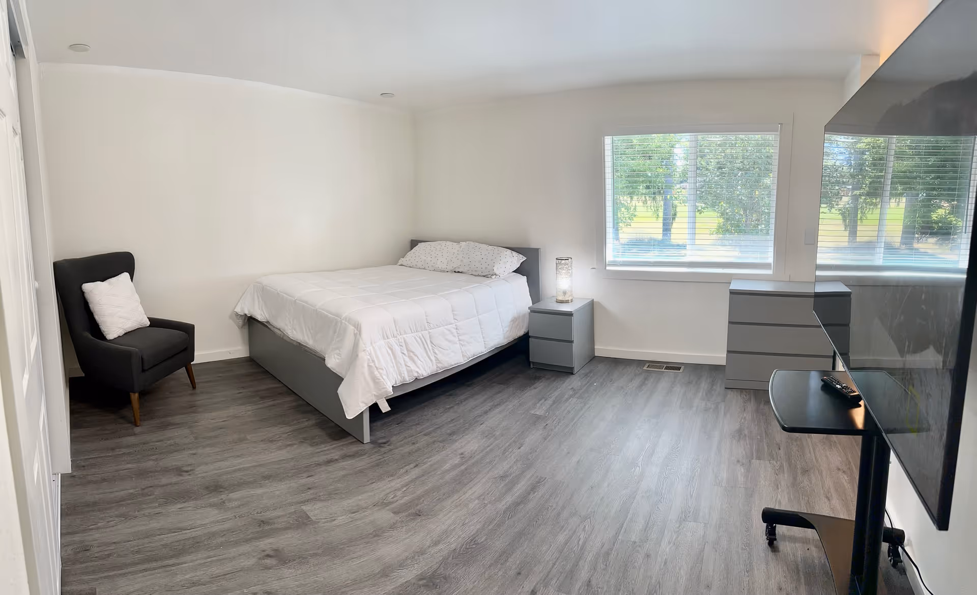 Minimal, modern bedroom with a bed, gray furnishings, window view, and wall-mounted TV.