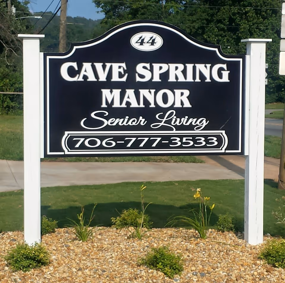 Front sign for Cave Spring Manor Senior Living with phone number on white posts.