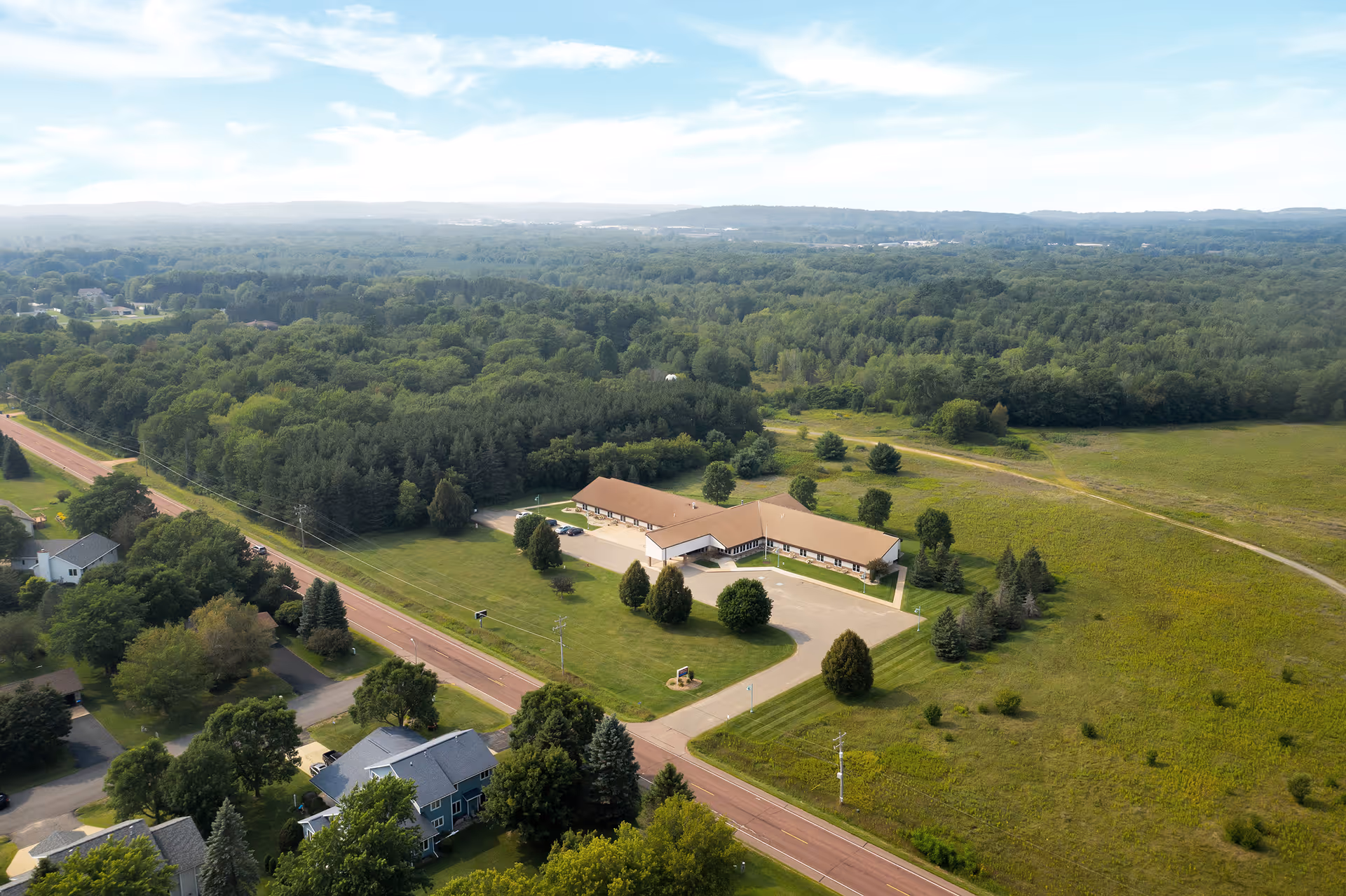 Aerial view of Wellington Place at Rib Mountain, a single-story facility amid green fields and parking.