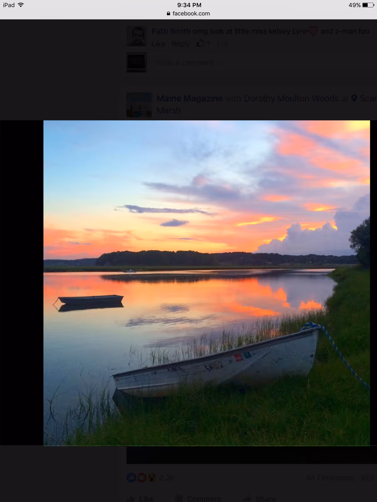 Sunset over a calm river with boats and grassy shoreline.
