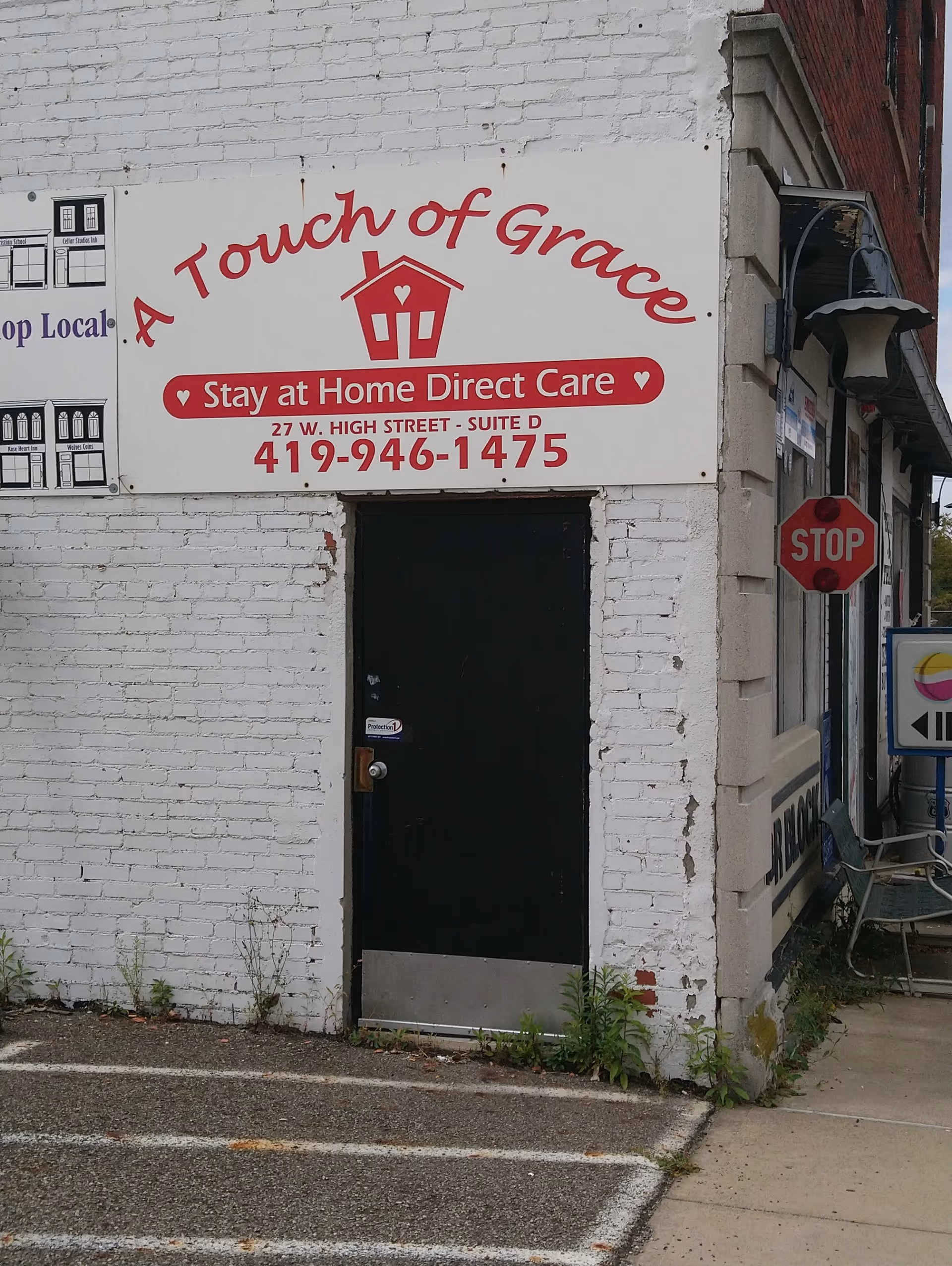 White brick building facade with red sign reading A Touch of Grace and a black door.