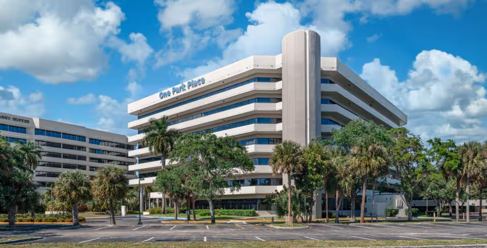 Front view of One Park Place senior living building with palm trees under blue sky.