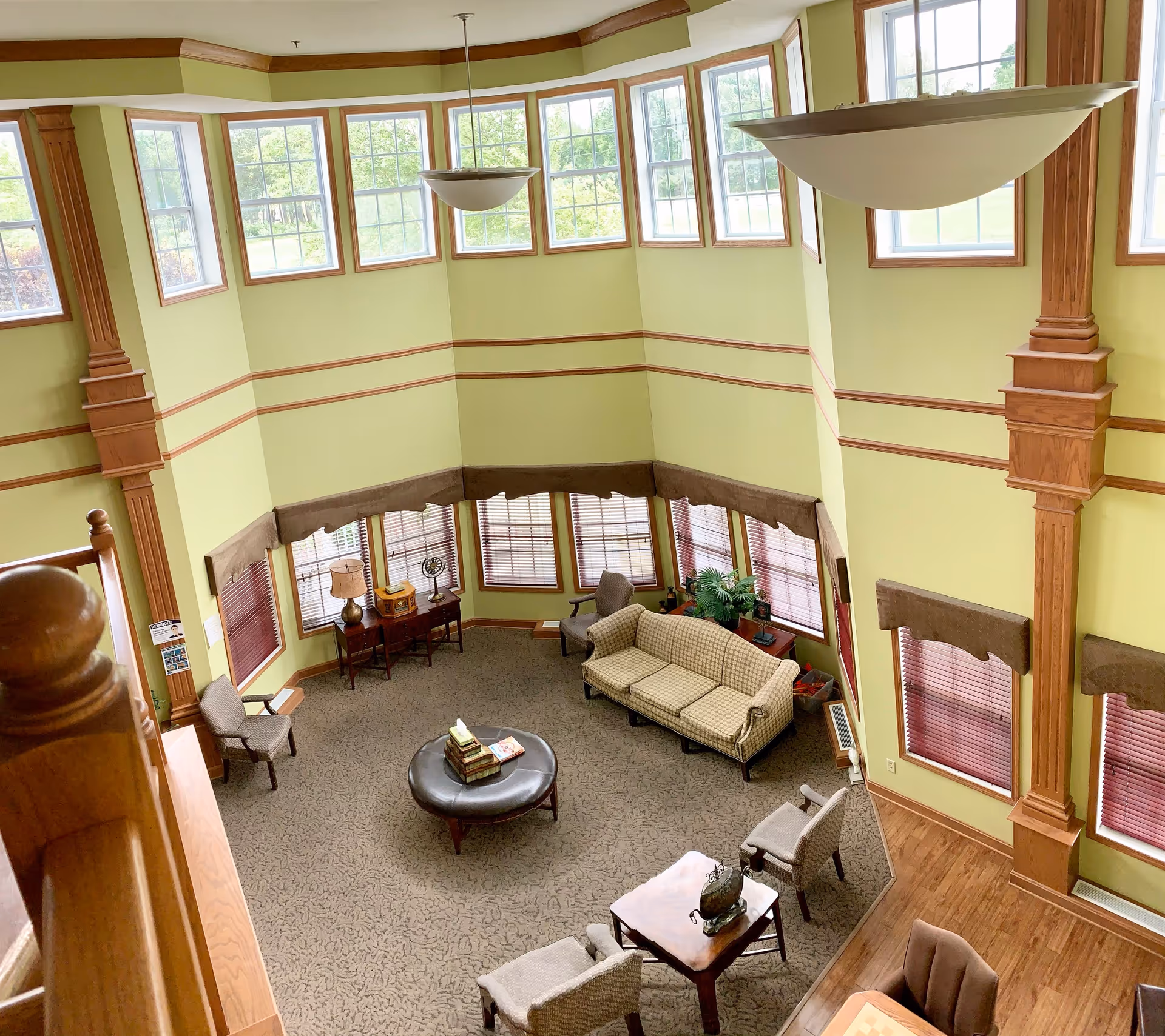 Two-story atrium lounge with lime-green walls, large windows, and wooden columns.