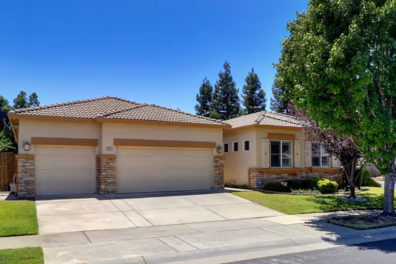 Front exterior of a beige assisted living building with three garage doors and landscaped yard.