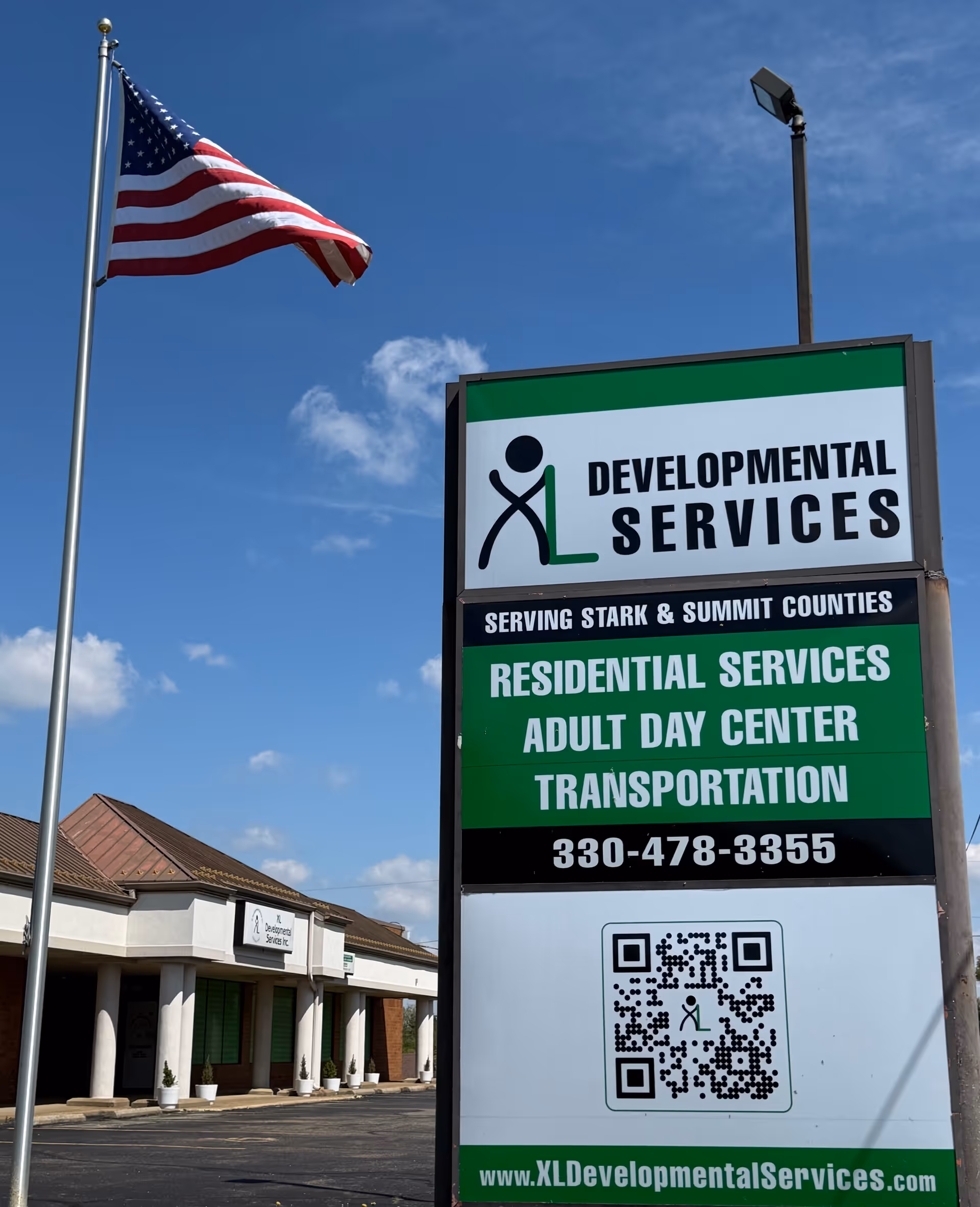 American flag beside a tall XL Developmental Services sign in front of a storefront building.