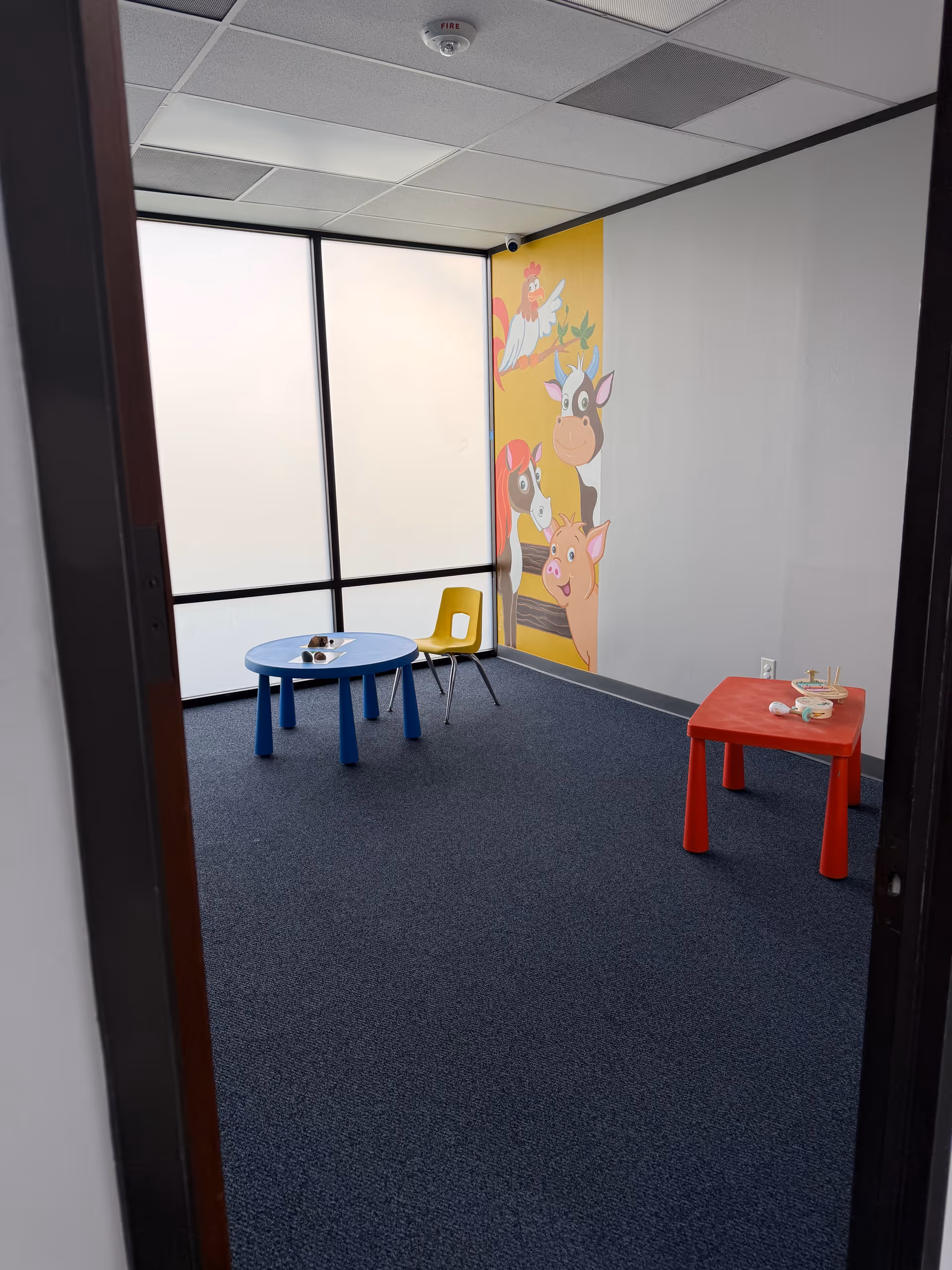 Small play area with blue and red tables, a mural, and frosted windows.
