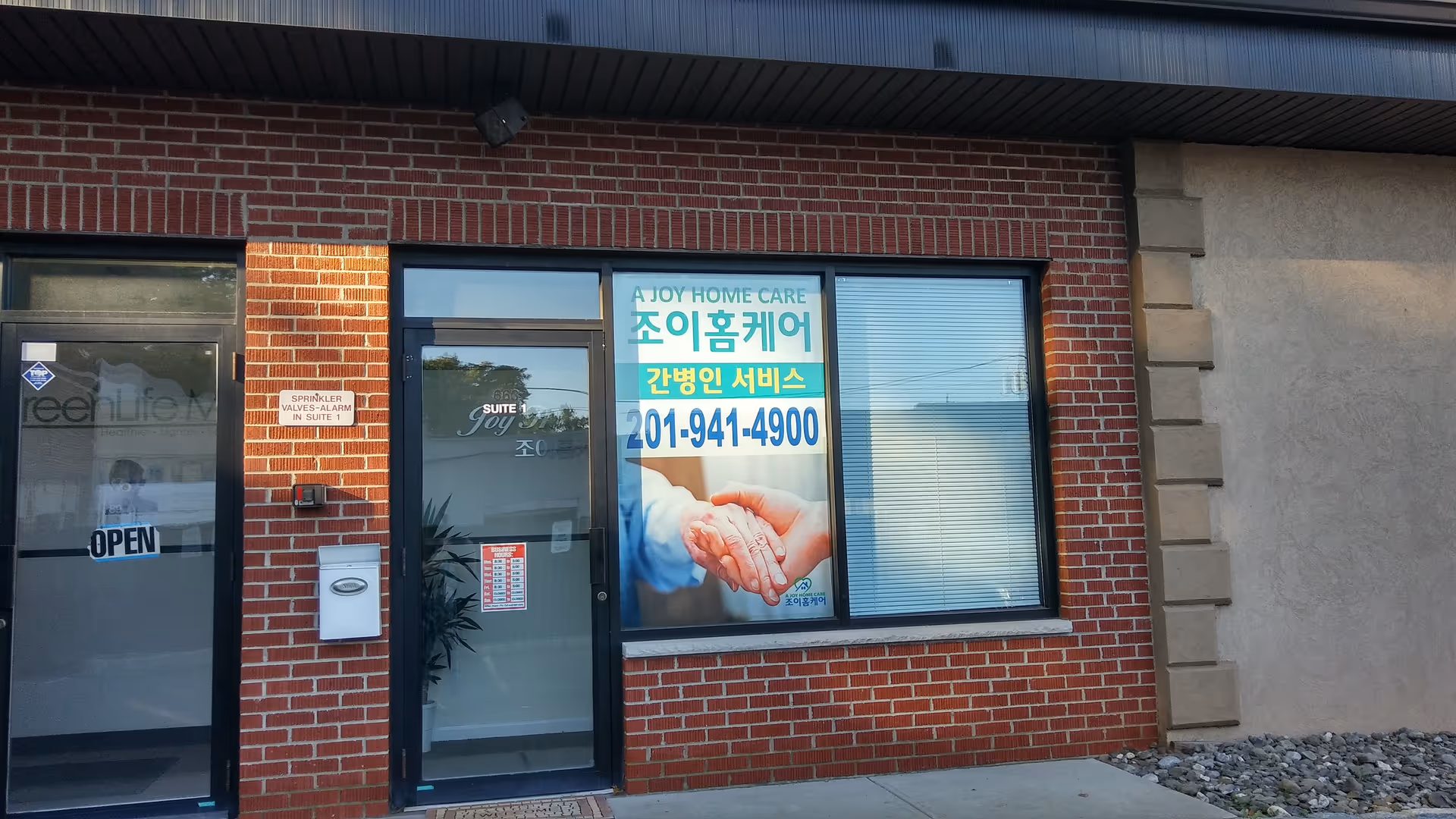 Brick building entrance with glass door and large window sign for A Joy Home Care.