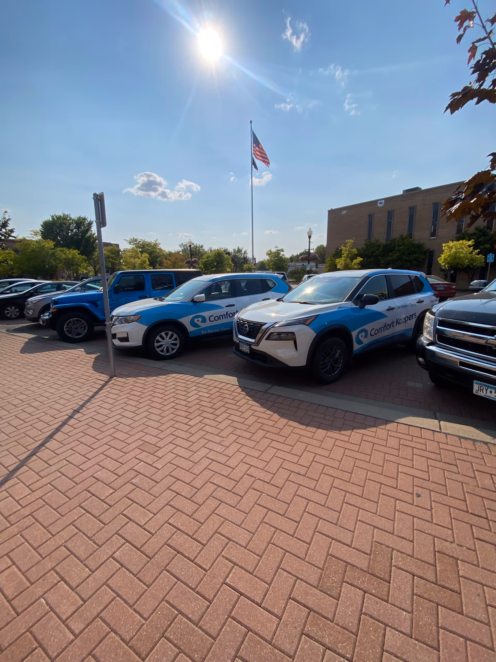 A row of Comfort Keepers vehicles parked in front of the facility on a sunny day.