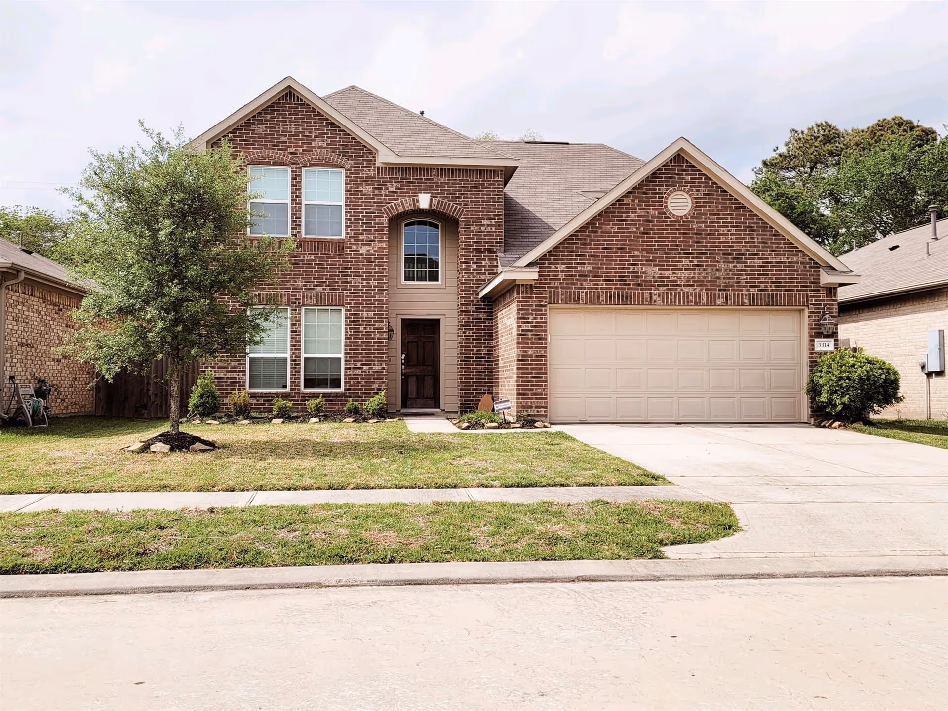 Two-story brick suburban house with a two-car garage and manicured lawn.