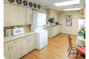Cozy senior living facility kitchen with light cabinets, appliances, and a small dining table and chairs.