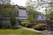 Two-story nursing home building with white siding, brown trim, trees, and a walkway.