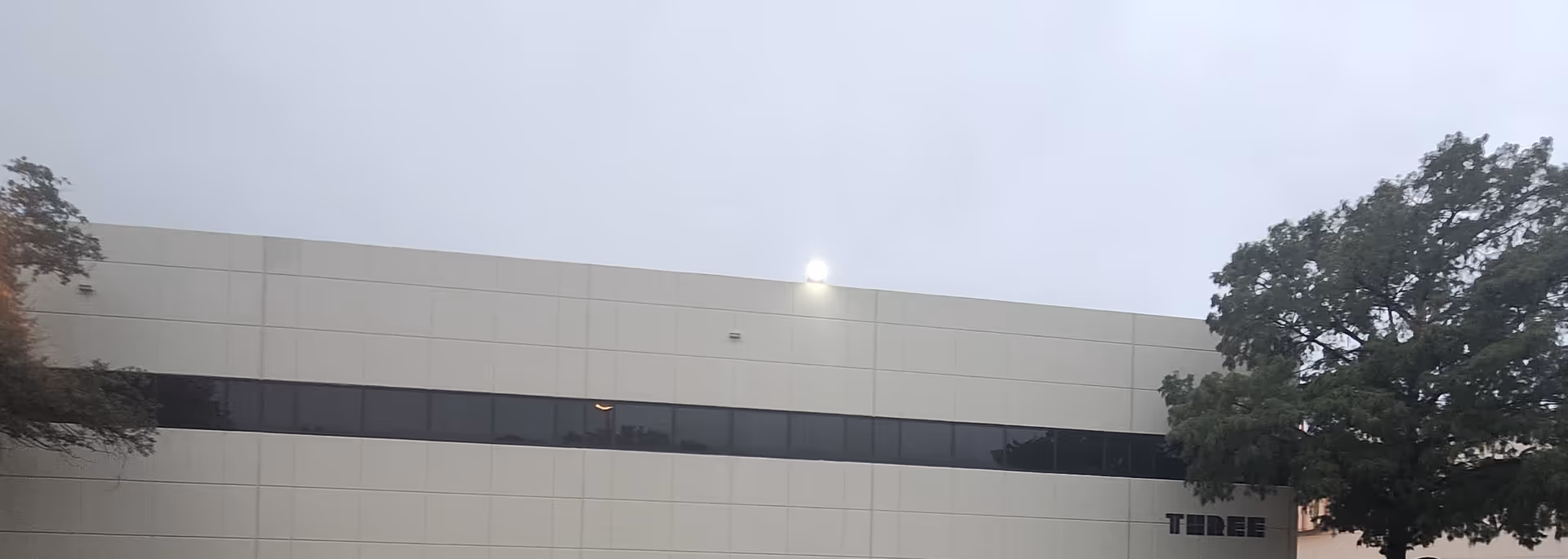 Exterior view of a beige facility building with a long dark window strip.