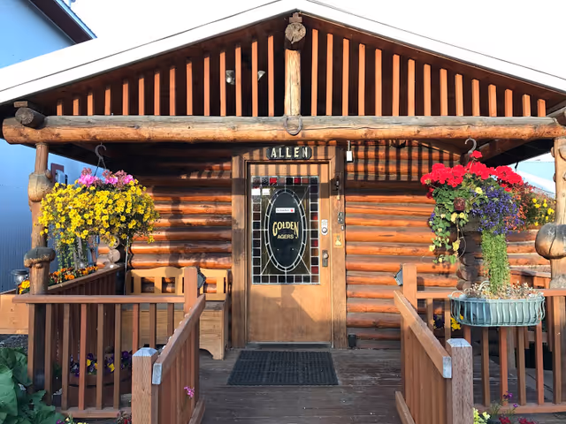 Log cabin-style entrance to Golden Agers Homecare with hanging flower baskets on a wooden porch.