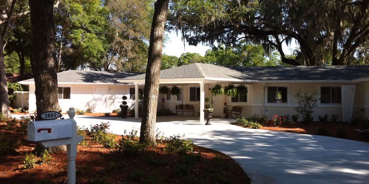 Single-story assisted living facility with a paved driveway, front entrance, benches, and landscaping.