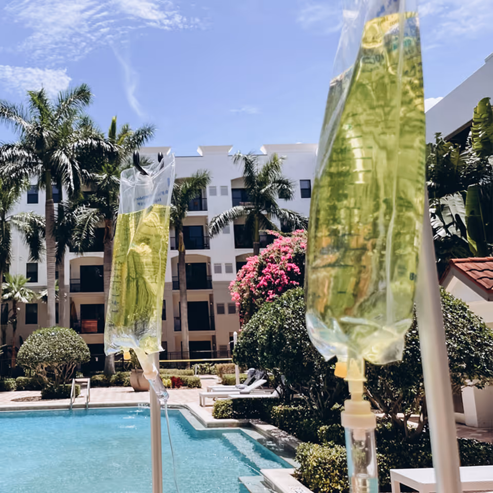 Outdoor pool area with palm trees and IV therapy bags in foreground.