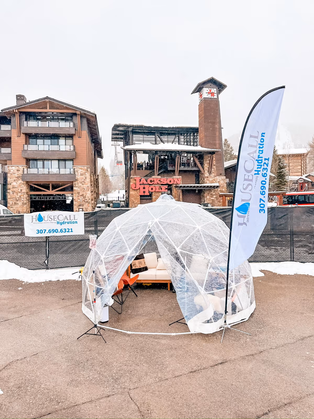 Clear dome tent with chairs outside, banners read House Call Hydration, Jackson Hole building in background.