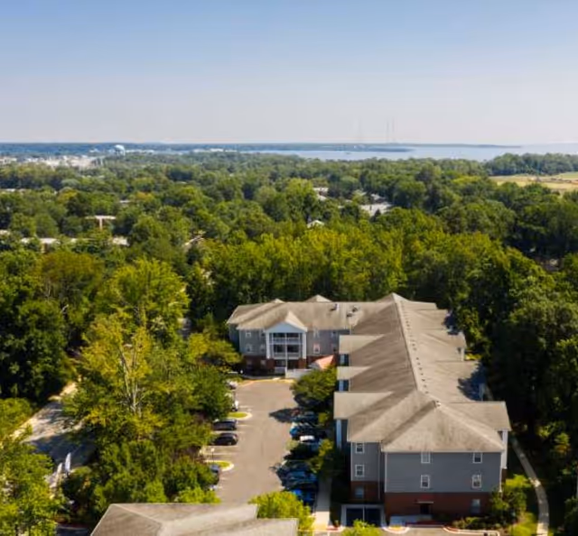 Aerial view of a senior living campus surrounded by trees with a distant water horizon.