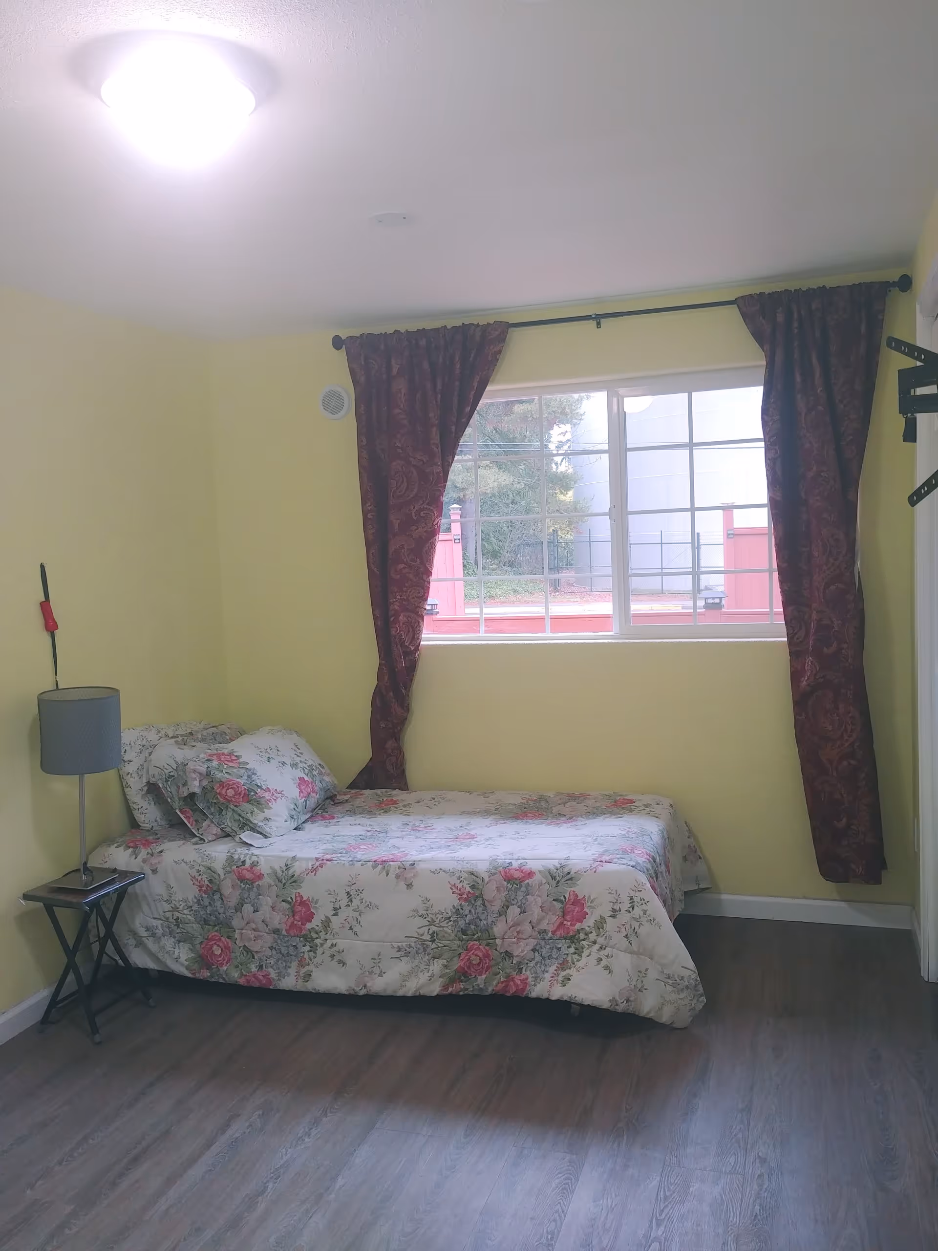 Yellow walls with a floral bed, nightstand, and window curtains.