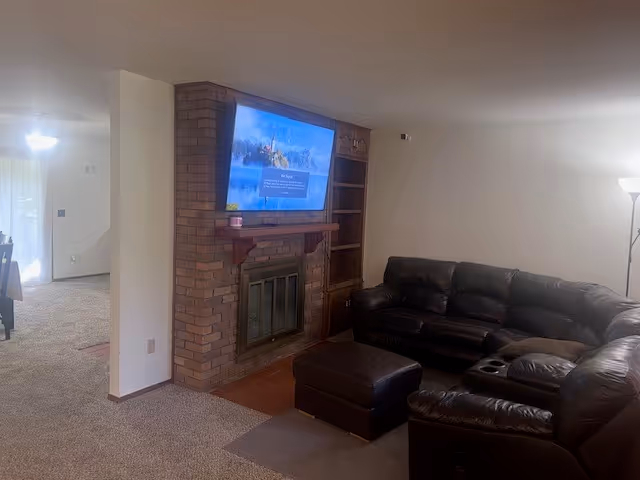 Living room with brick fireplace, mounted TV, leather sectional, and built-in shelves.