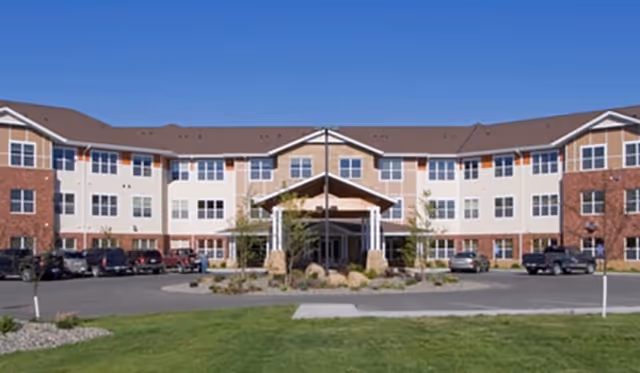 Exterior view of a multi-story senior living facility with a central entrance and parking.