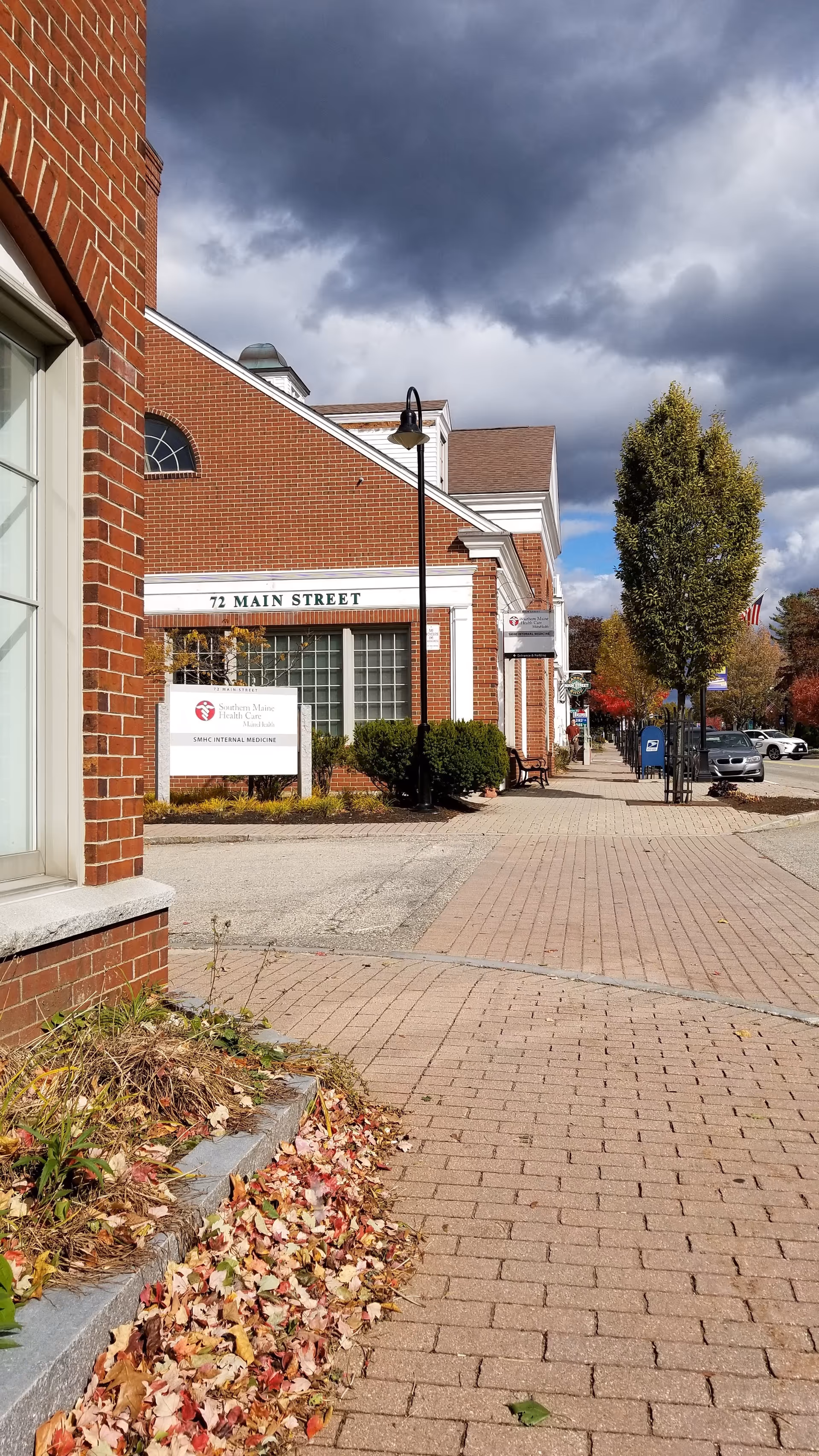 Brick medical center on Main Street with sidewalk, signage, and autumn leaves.