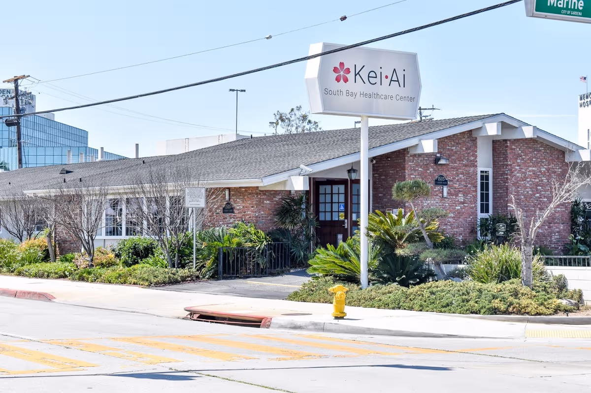 Exterior view of Kei-Ai South Bay Healthcare Center with brick facade and landscaping.