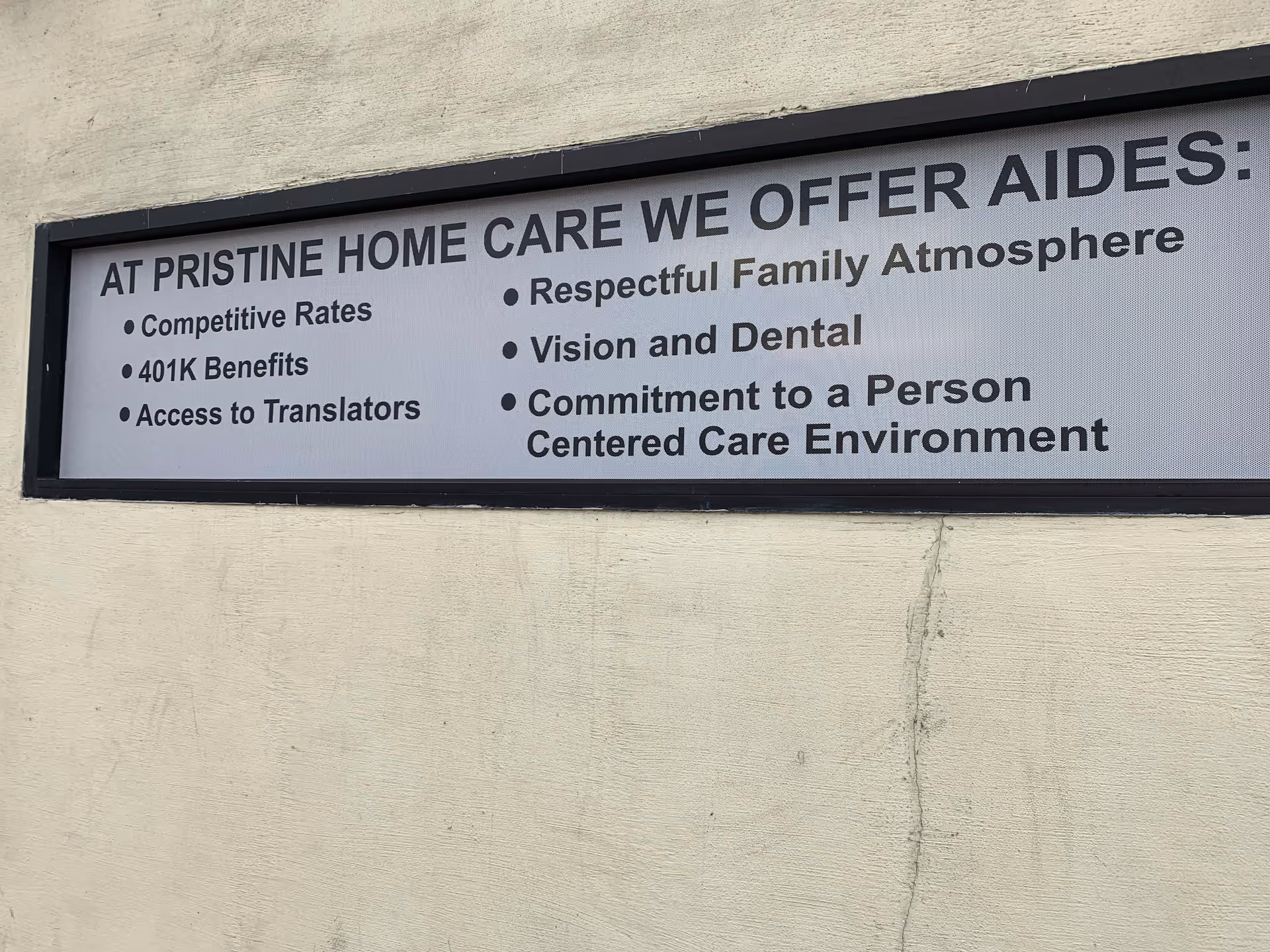 Large exterior sign on a beige wall listing Pristine Home Care services and benefits.