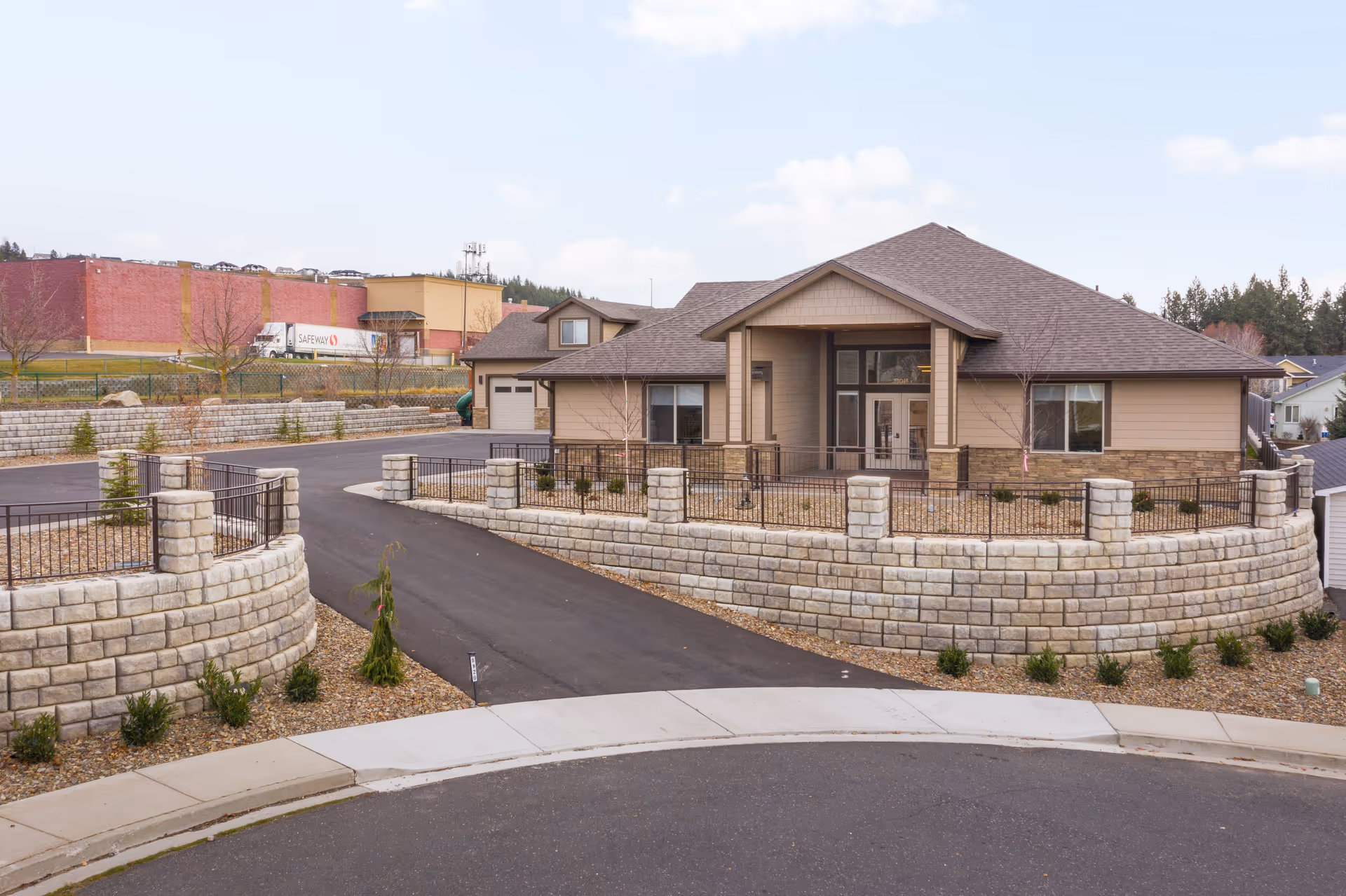 Single-story beige senior living facility with stone retaining walls, driveway, and gated entrance.
