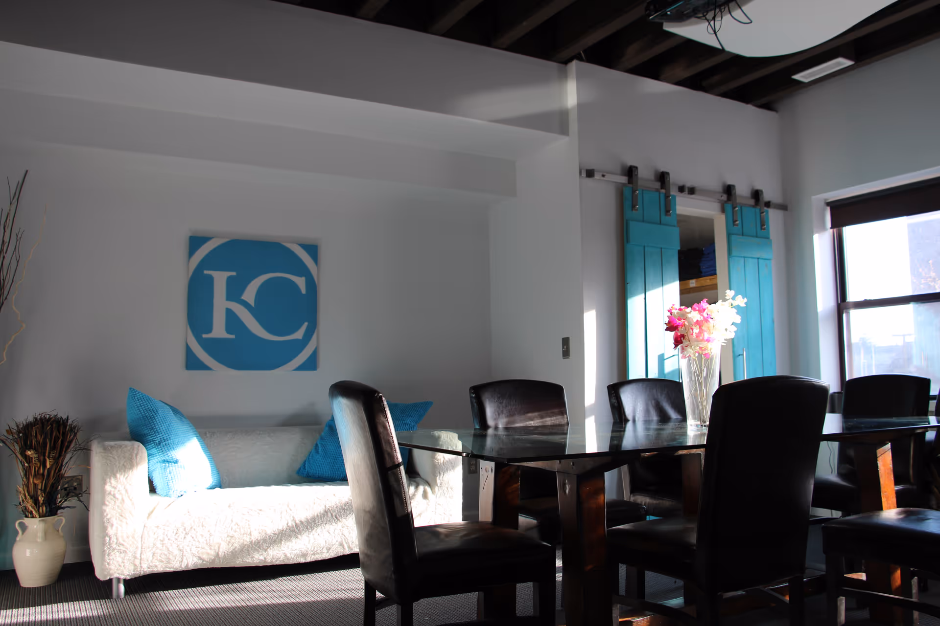 Bright dining area with glass table, black chairs, sofa with blue pillows, and turquoise doors.