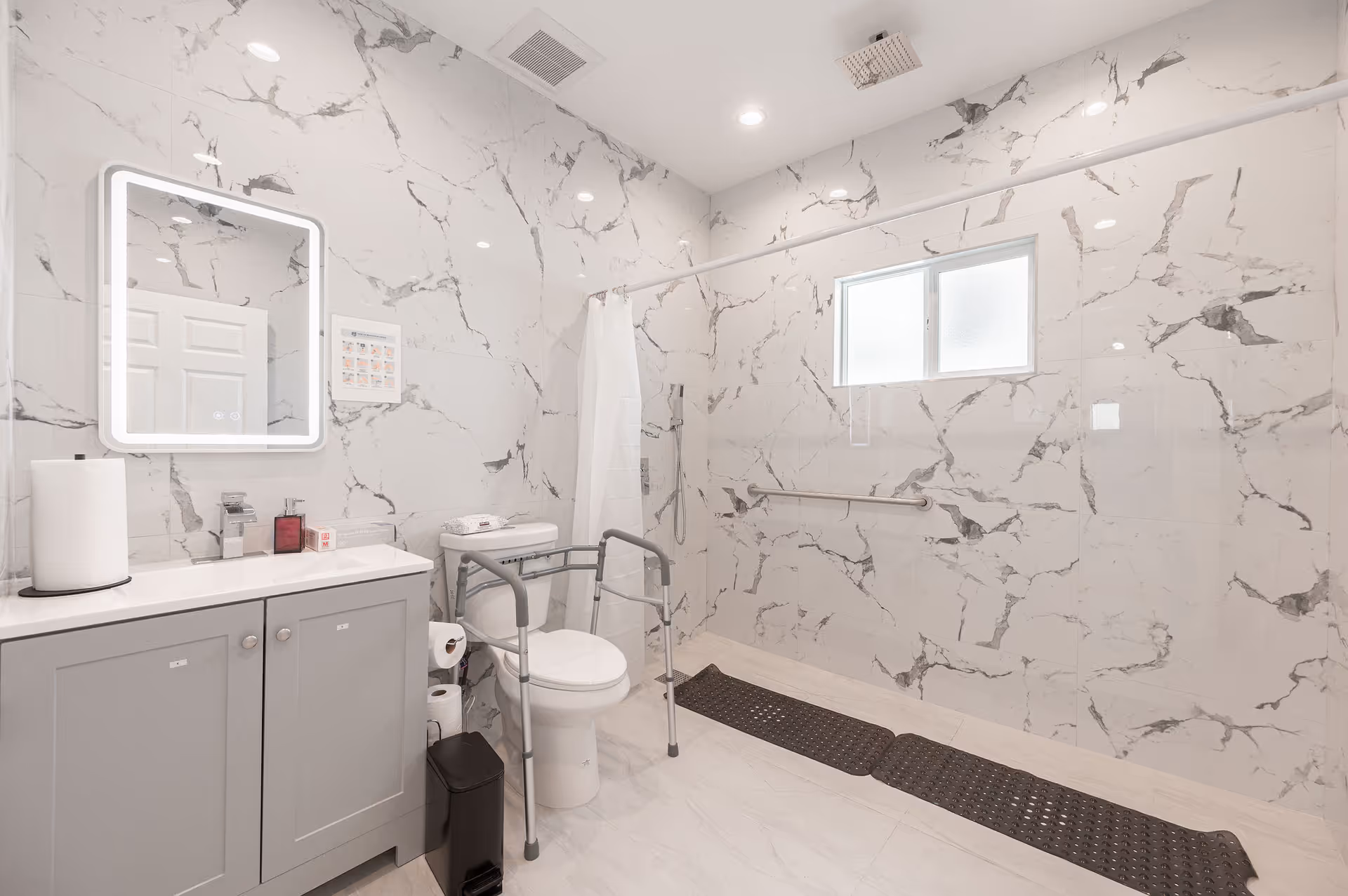 Accessible bathroom with marble walls, a mirror, sink, toilet, and grab bars.