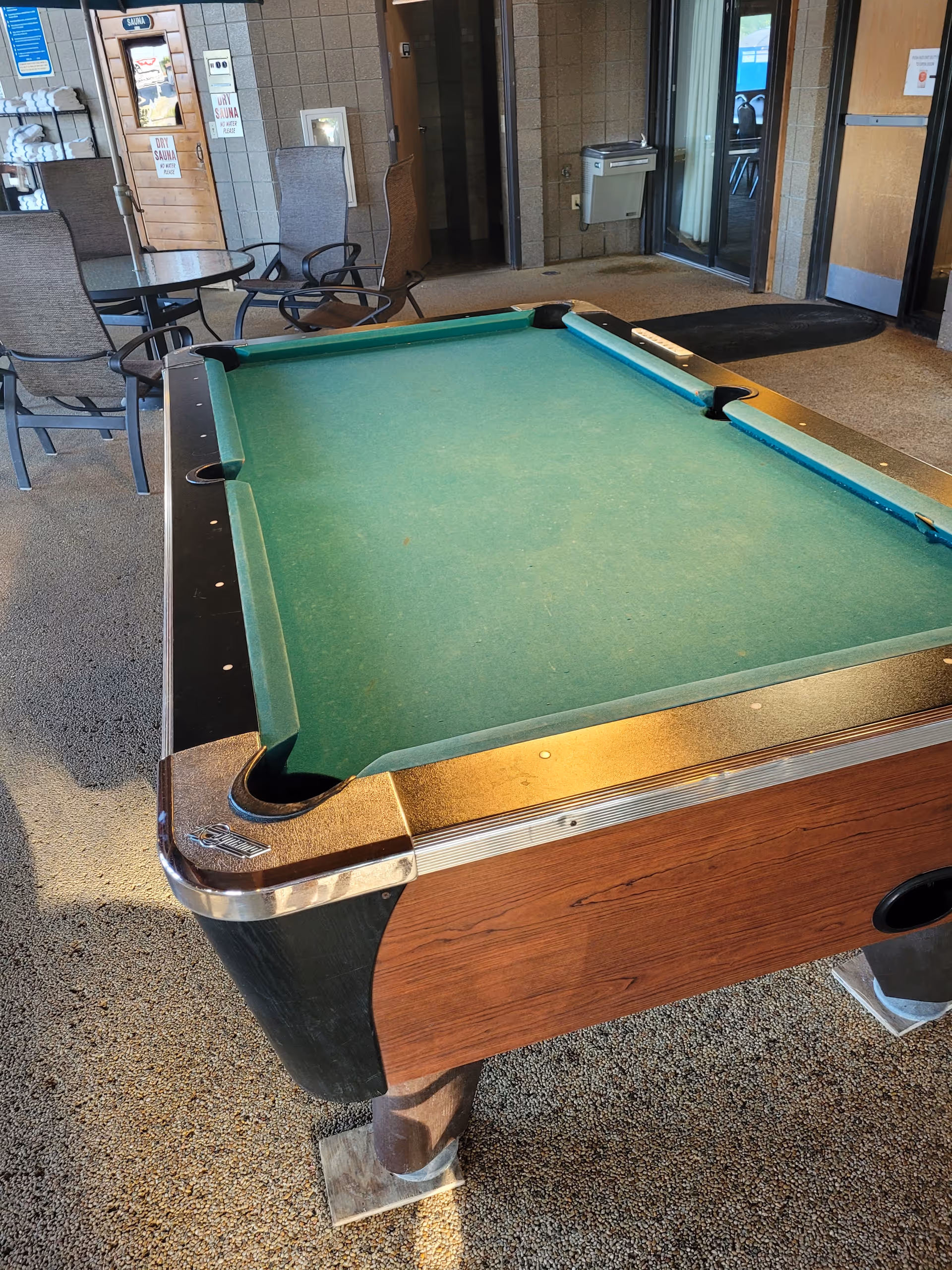 Indoor lounge area with a green pool table and surrounding chairs near glass doors.