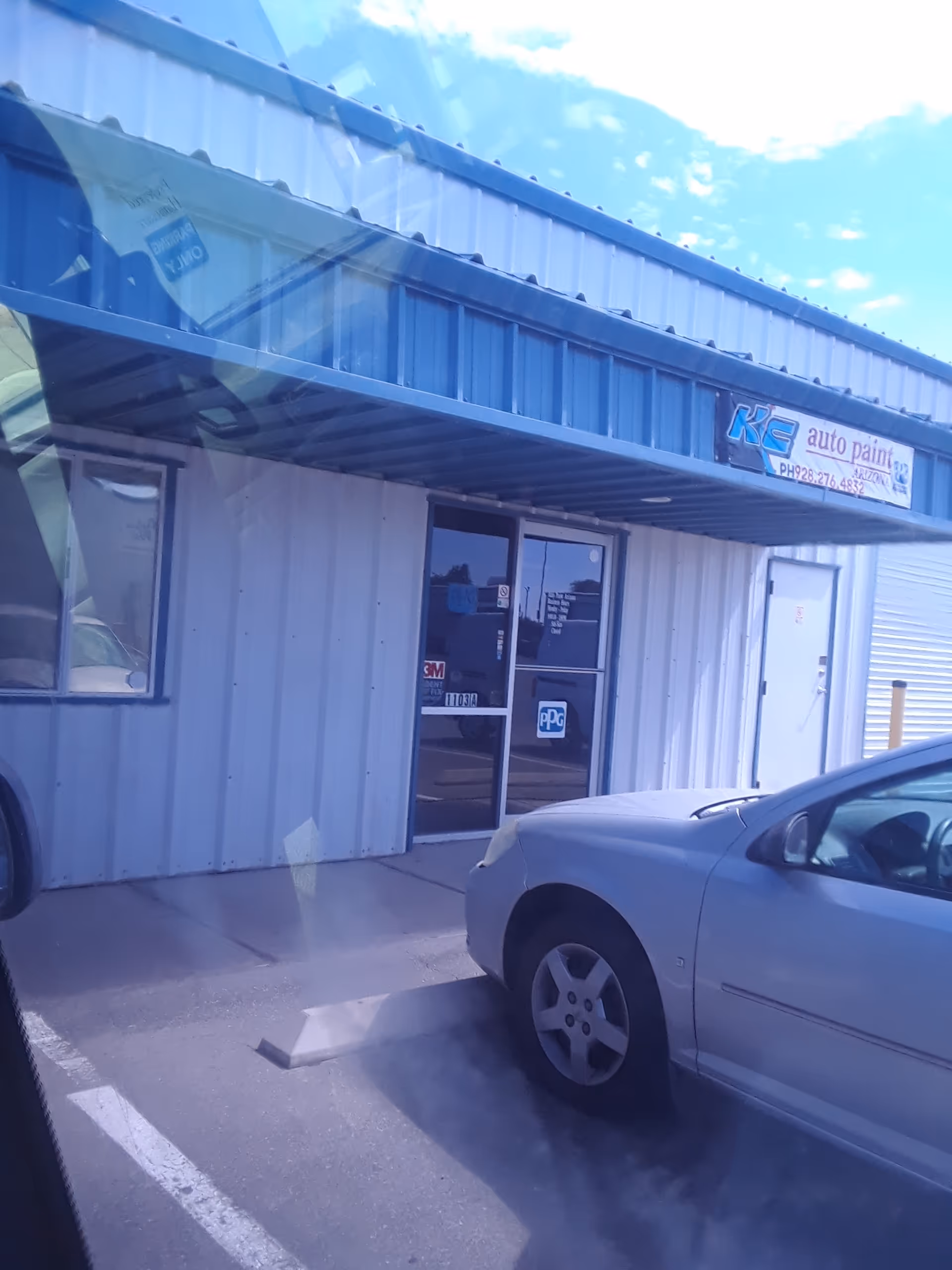 Blue metal exterior of a storefront with glass doors and parked cars.