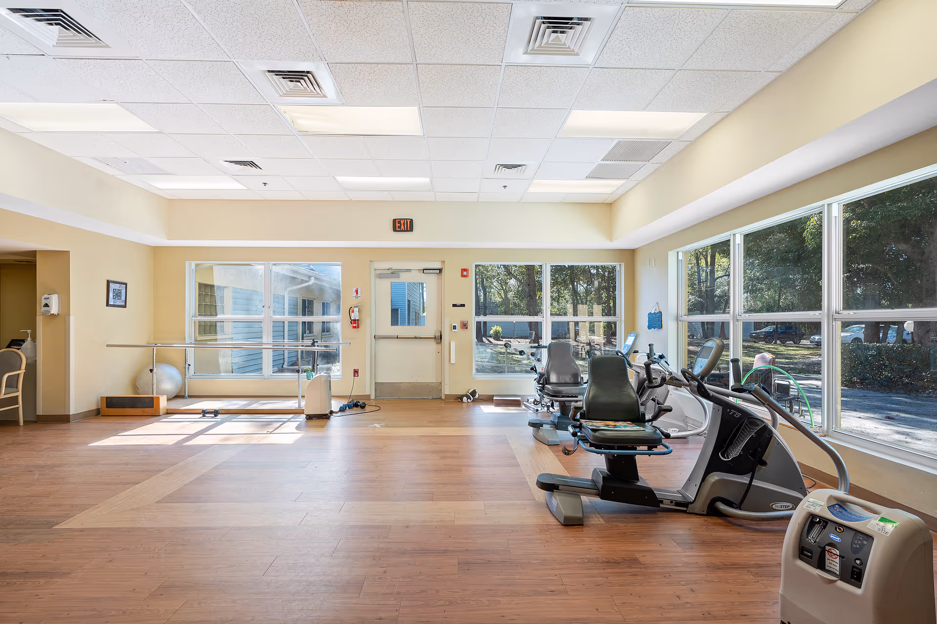Bright indoor fitness room with exercise equipment and large windows.