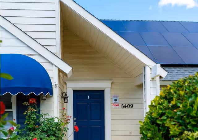 Front entrance of a beige senior living facility with blue door, awning, and shrubs.